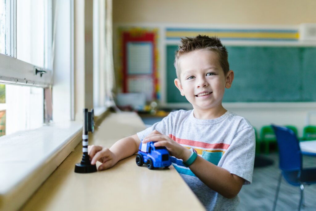 A happy child enjoys playing with a toy car in a bright classroom setting.