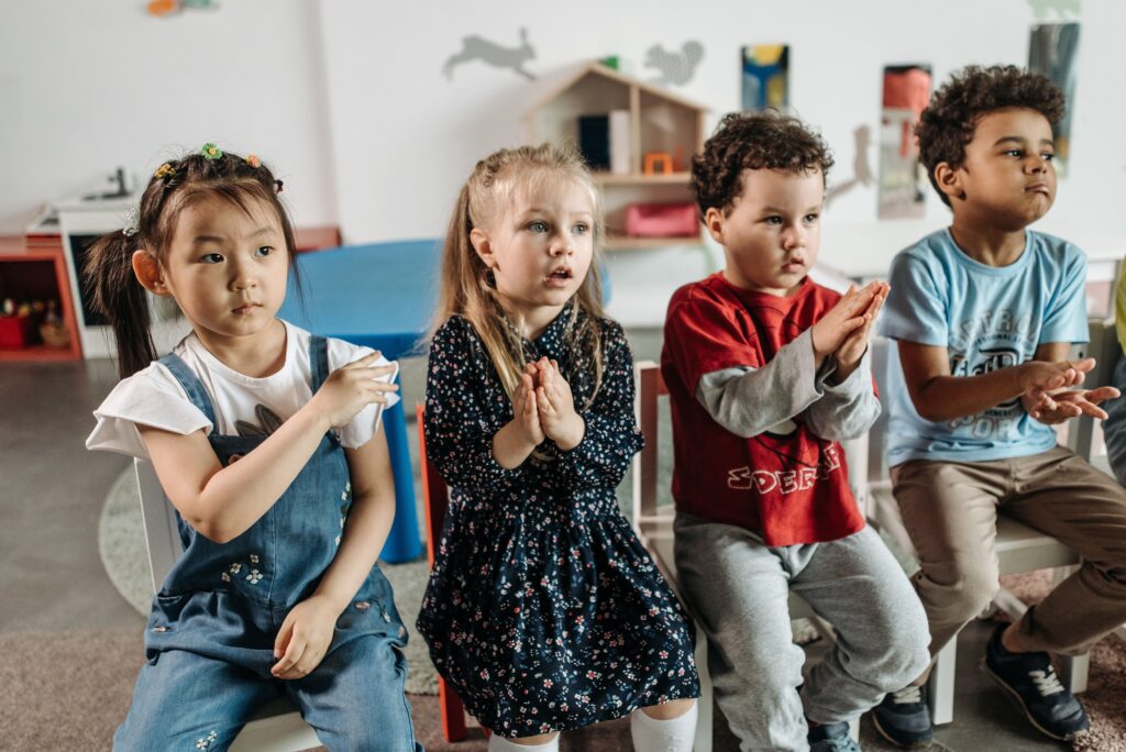 A diverse group of children clapping in an engaging kindergarten classroom setting.