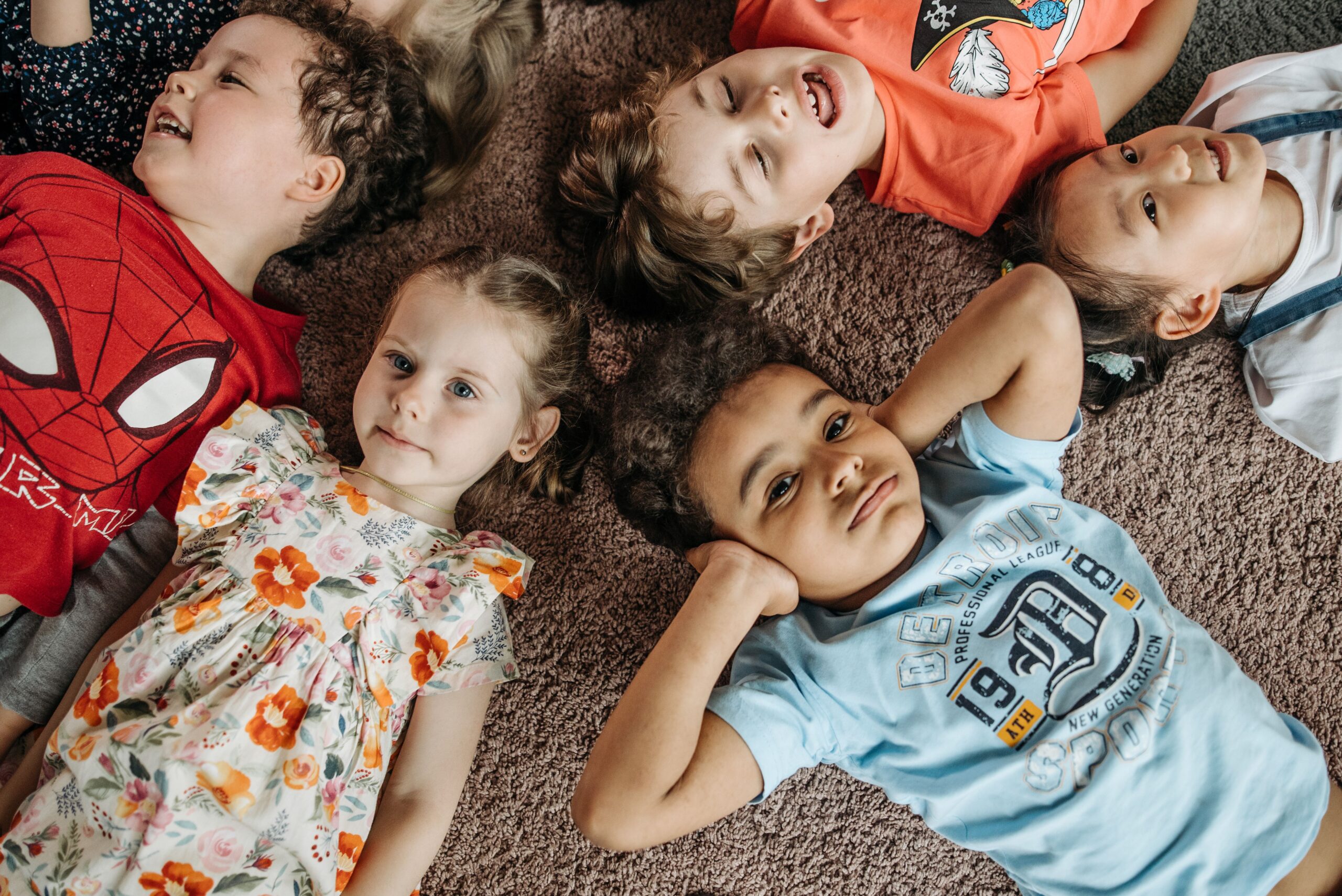 Home A cheerful group of diverse children lying playfully on a carpet indoors.