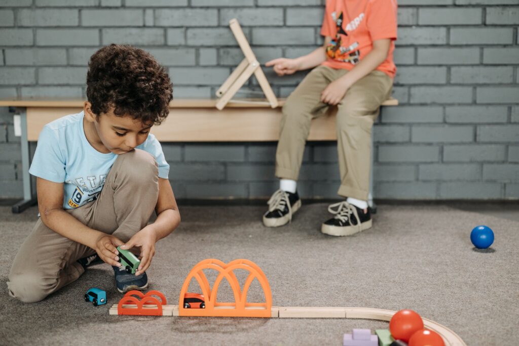 Two kids enjoying creative play with wooden toy tracks in a classroom setting.