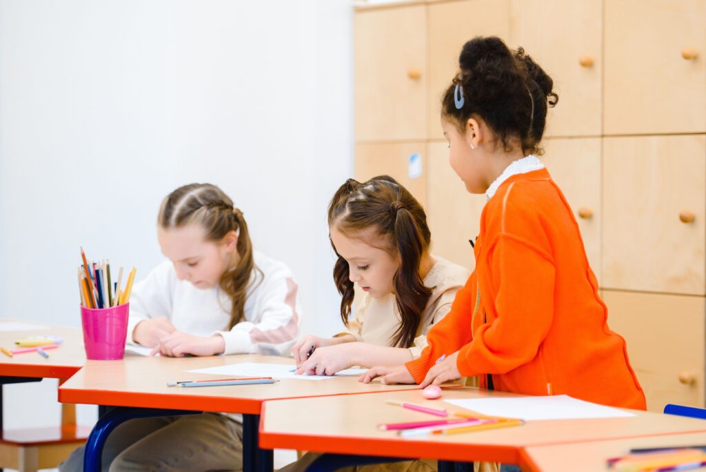 Three girls participate in a creative drawing session at a classroom table.